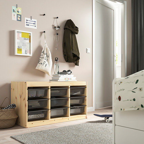 Mueble de almacenaje TROFAST con cajas de malla en color beige junto a una cuna, con estructura de madera clara, ideal para la habitación de los niños.