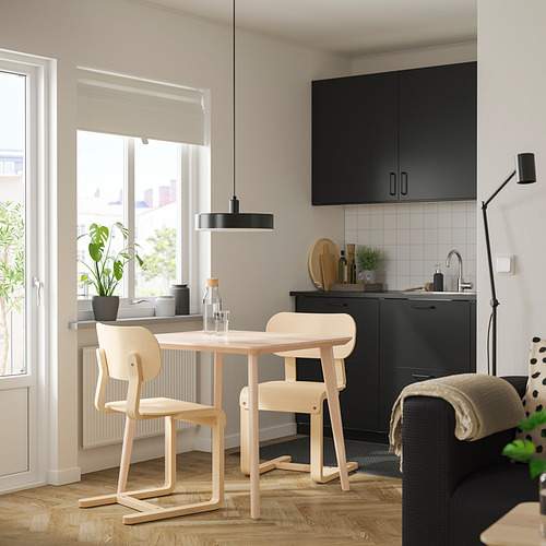 Cocina moderna con armarios negros, mesa de madera y sillas ligeras junto a la ventana, acogedora y bien iluminada.