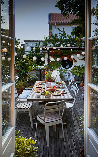 Ingeniosas cenas al aire libre: mesa de acacia, sillas grises, terraza iluminada por la vegetación, vista urbana.