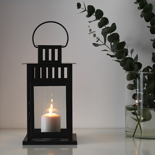 Linterna negra con vela brilla para un ambiente acogedor. Colocado sobre la mesa con eucalipto en jarrón.