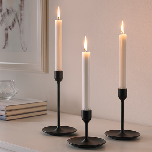 Tres candelabros negros de diferentes alturas, cada uno sosteniendo una vela blanca encendida, dispuestos sobre una mesa.