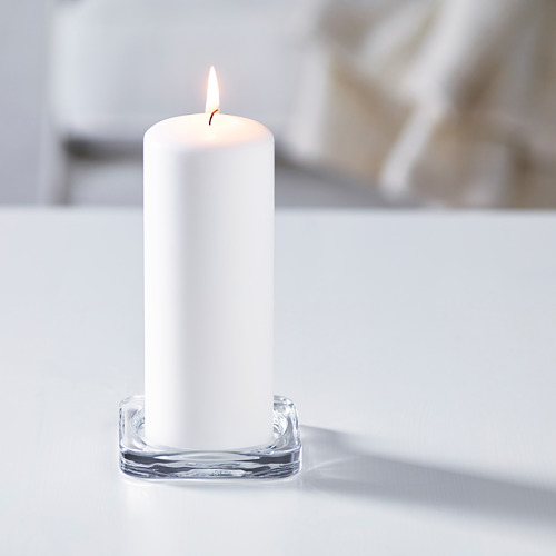 Una vela blanca encendida en un soporte de vidrio transparente, creando ambiente.