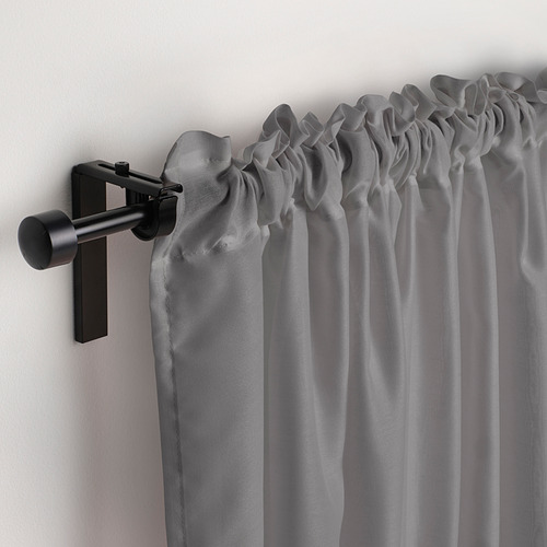 Las cortinas transparentes de color gris claro cuelgan de una varilla moderna en negro mate, difuminando suavemente la luz del día.