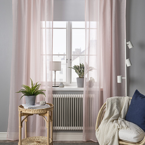 Acogedor rincón con cortinas rosas transparentes STENFRÖ, una mesa de mimbre y un sillón. Las cortinas difunden suavemente la luz, complementando la decoración moderna.
