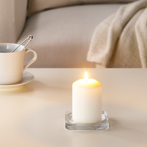 Vela blanca encendida en un soporte transparente junto a la taza de café blanco, creando un ambiente acogedor.