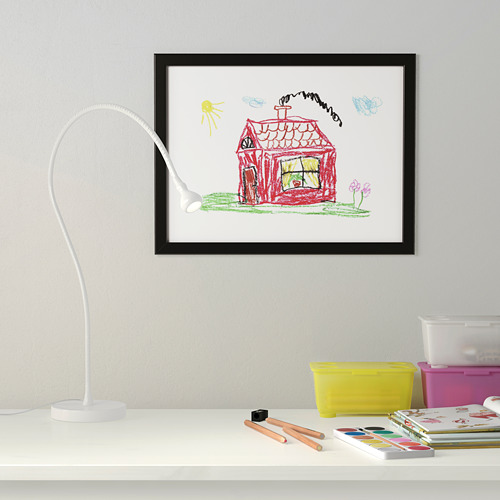 El dibujo enmarcado de los niños cuelga de la pared con una lámpara ajustable debajo, escritorio con materiales de arte.