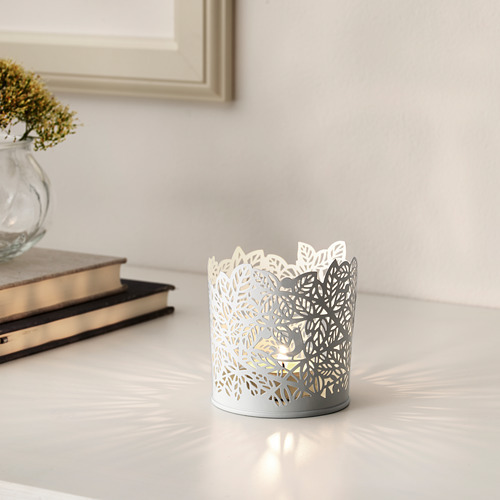 Portavelas con recorte de hojas, a la luz de las velas. Cerca de allí, las flores secas y los libros crean una decoración acogedora.