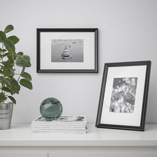 Los marcos negros muestran fotos de veleros y mariposas. Planta, libros, esfera en estante blanco.