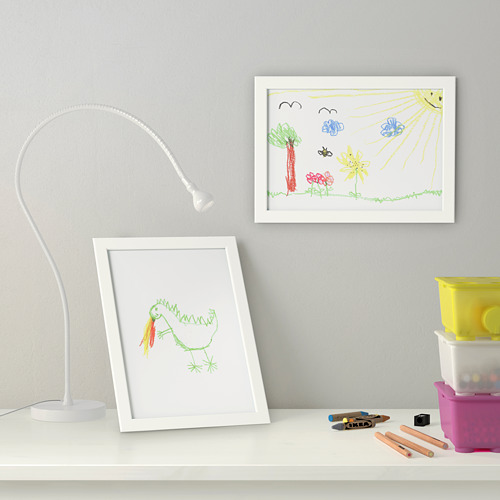 Dibujos de niños en marcos blancos sobre escritorio. Lámpara, materiales de arte y almacenamiento cercano.