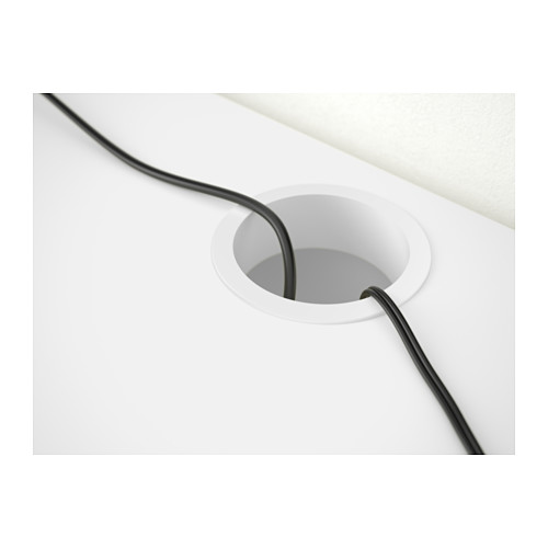 Escritorio blanco con cable negro cuidadosamente alimentado a través de un orificio de cable circular para una configuración organizada.
