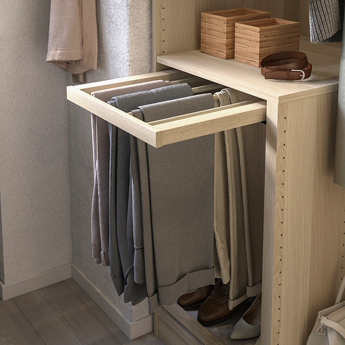 La percha para pantalones KOMPLEMENT sostiene pantalones grises en un estante de madera clara.