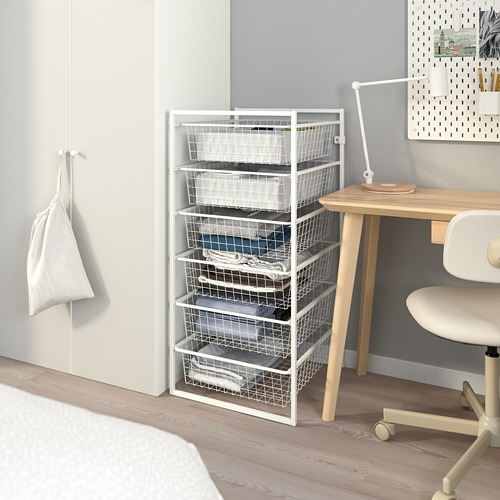 Mueble de almacenaje JONAXEL blanco con seis cajones, colocado junto a un escritorio de madera y una silla. Ideal para organizar artículos en cualquier habitación.