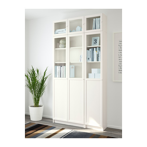 Librería BILLY blanca con puertas de cristal y paneles. Muestra libros y oculta el desorden. Anclado a la pared para mayor estabilidad.