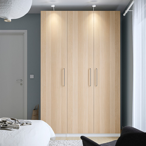 Armario de madera PAX centrado contra una pared gris, más alto que la cama.