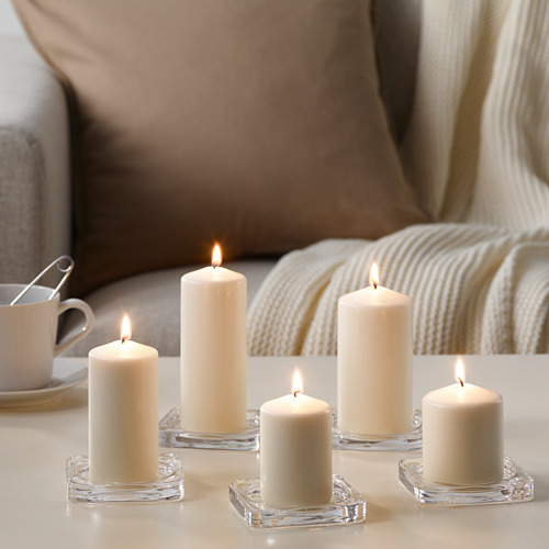 Seis velas blancas en soportes de vidrio transparente, encendidas, sobre una mesa de color claro, creando un ambiente cálido y acogedor.