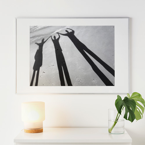 Sombras en blanco y negro de tres personas tomadas de la mano, enmarcadas y exhibidas en una pared sobre una mesa con una lámpara y una planta.