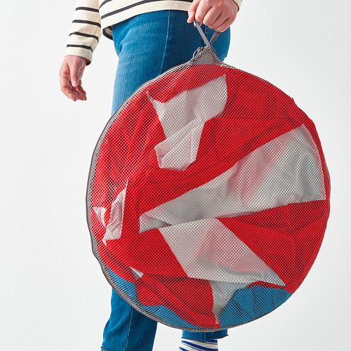Persona que sostiene un gran círculo de malla roja con tela blanca en su interior, probablemente una carpa de juegos para niños.