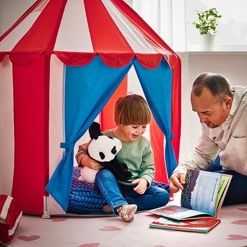 Un niño se sienta dentro de una colorida carpa de juego con un hombre leyendo un libro, ilustrando un acogedor escondite donde los niños pueden jugar o escuchar cuentos.