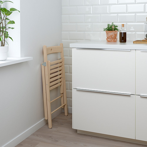 Silla plegable de madera apoyada en un mueble de cocina blanco, con una planta en maceta y una botella de aceite en la encimera.