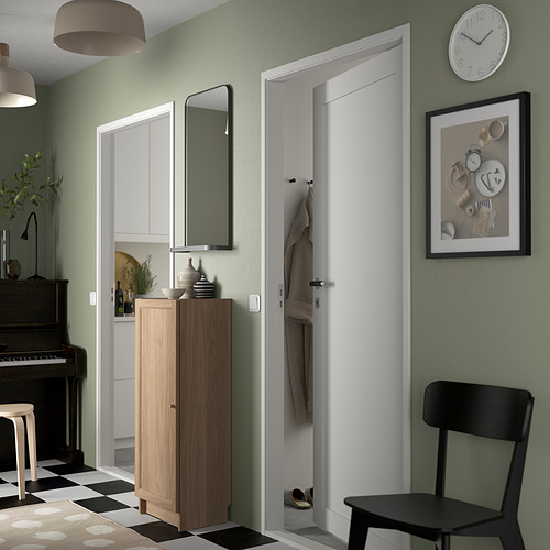 Elegante pasillo con librería BILLY en madera natural contra pared verde, junto a una estrecha puerta blanca.