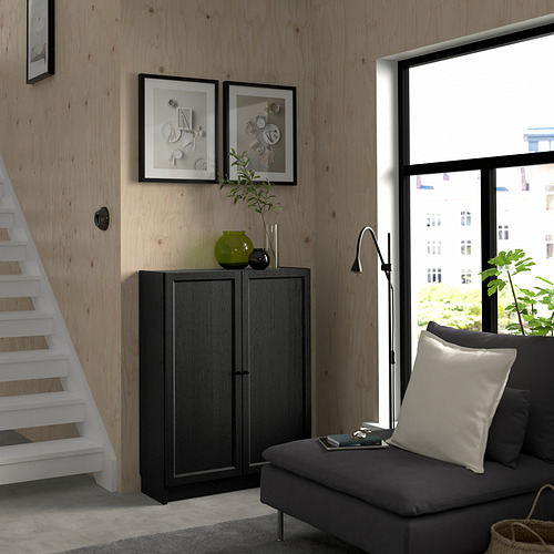 Sala de estar moderna con gran ventanal, sofá gris, estantería BILLY y escaleras. Decorado con arte y plantas.