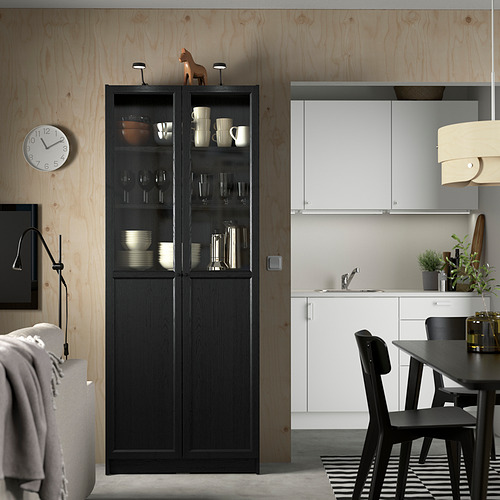 Mueble BILLY negro en cocina minimalista, casi juego de comedor blanco, con puertas de vidrio que muestran platos.