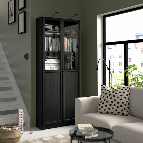 Librería BILLY con libros, decoración, cerca de las escaleras. Sofá gris, vista a la ciudad, lámpara, planta.