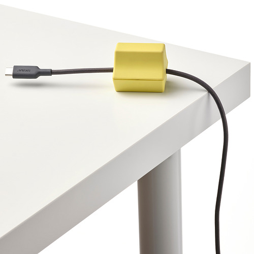Un ancla USB de color amarillo brillante sostiene cuidadosamente un cable negro sobre un elegante escritorio blanco, mostrando su calidad organizativa.