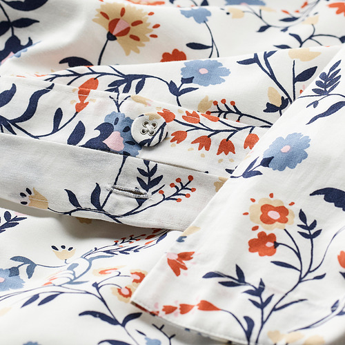 Edredón floral en primer plano; Crema con estampados florales azul marino y rojo, con esquinas abotonadas. Algodón orgánico suave y transpirable.