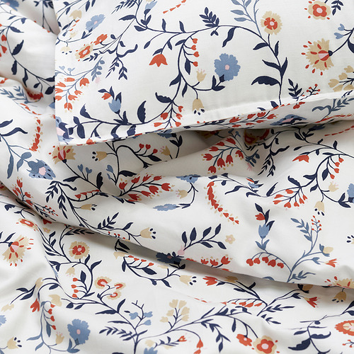 Conjunto nórdico floral, suave algodón orgánico, blanco con flores azules, naranjas y beige, doblado cuidadosamente.
