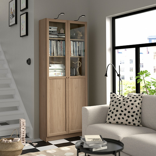 Sala de estar con estantería BILLY marrón claro, libros, decoración, escalera, sofá blanco y mesa de centro con planta.