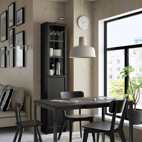 Comedor moderno con mesa negra, sillas, gabinete BILLY, lámpara, reloj, sofá, planta.