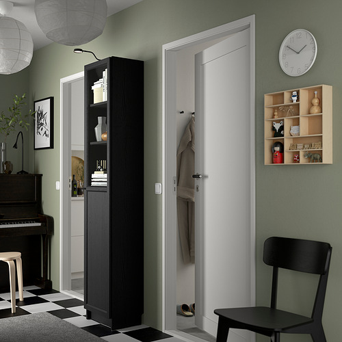 Librería BILLY en negro al lado de la puerta, llena de artículos, puerta de panel, silla, estante de madera en pared verde.
