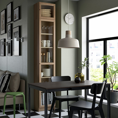 Comedor moderno con almacenamiento de madera alto BILLY, pared verde, sillas negras, mesa, lámpara de firma, pared de galería de arte, ventana grande y plantas.