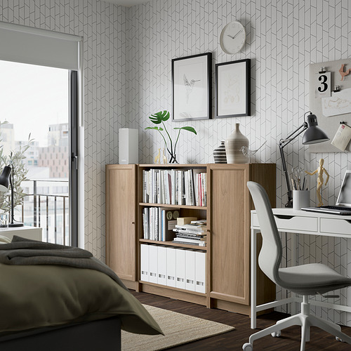 Moderna oficina en casa con estantería, escritorio y silla BILLY. La estantería tiene libros, el escritorio tiene computadora, vista de la ciudad a través de la ventana.