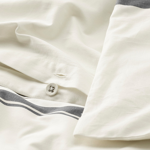 Primer plano de la ropa de cama blanca nítida con tiras grises, detalle de botones visible.