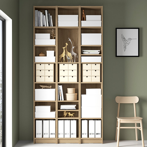 Estantería alta BILLY con cajas de almacenamiento blancas y de madera y artículos decorativos. Frente a un muro verde.