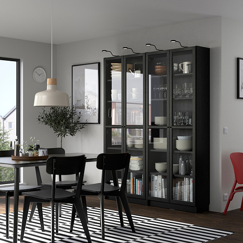 Comedor moderno con librería BILLY negra, sillas y lámpara. Ventana grande, alfombra a rayas y silla de acento rojo.
