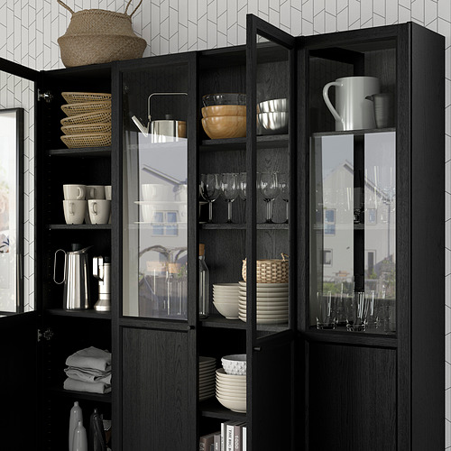 Estantería de madera oscura con puertas de vidrio, exhibiendo tazas, cuencos y copas de vino. Los estantes ajustables sostienen cestas tejidas y toallas cuidadosamente dobladas.
