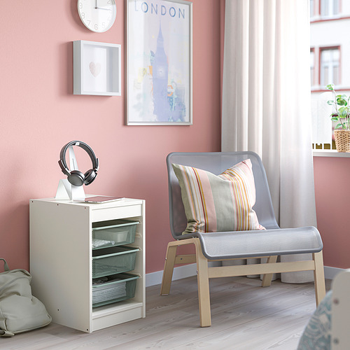 Pequeño mueble de almacenaje TROFAST blanco junto a una silla gris con almohada a rayas. Los auriculares están en la parte superior. Suelo de madera clara.