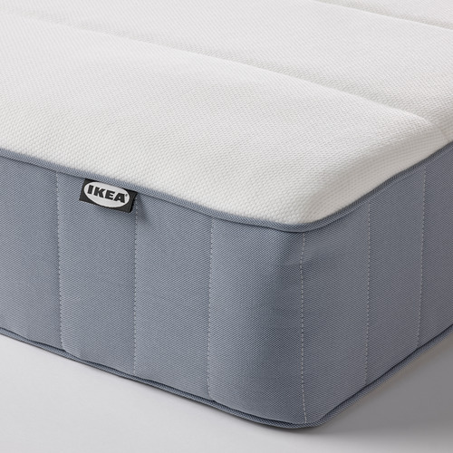 Primer plano del colchón de IKEA que muestra la parte superior de espuma firme, los lados grises cosidos sin costuras y la etiqueta visible de la marca.