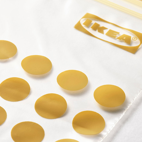 Múltiples sellos circulares dorados de ikea ISTAD esparcidos sobre una superficie blanca, con la etiqueta de la marca ikea visible en el fondo.