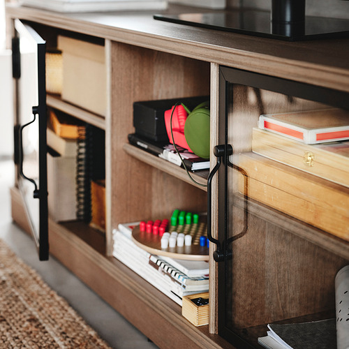 Mueble de tv de madera con manijas de metal negro y puertas de vidrio, para guardar aparatos electrónicos y material de oficina.