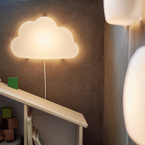 Lámpara UPPLYST en forma de nube en la pared, que ilumina libros y juguetes con un brillo cálido.