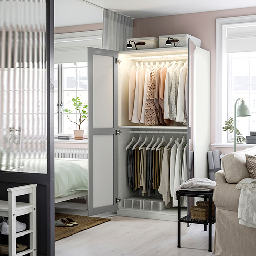 Un armario moderno, PAX, con puertas de espejo que reflejan un dormitorio acogedor. Cuenta con secciones colgantes y estanterías, que ofrecen abundante espacio de almacenamiento con un diseño elegante.