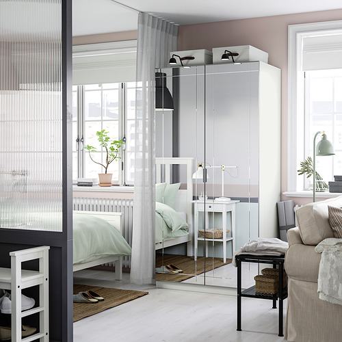 Dormitorio moderno con gran armario blanco PAX, puertas con espejos, cama acogedora, sofá y luz natural.