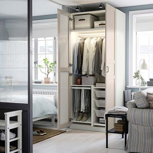 Armario abierto que muestra ropa, estantes y cajas de almacenamiento, con puerta de espejo que refleja la cama y la ventana.