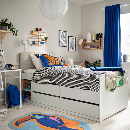 Dormitorio con cama blanca, cortinas azules, alfombra de colores y estantes flotantes.