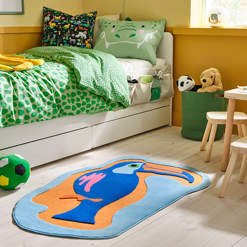 Una habitación para niños con una cama blanca, ropa de cama verde, una alfombra azul y una cesta de juguetes.