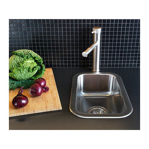 Fregadero de cocina moderno en acero inoxidable, diseño elegante con grifo, verduras en tabla de cortar, placa para salpicaduras de azulejos de rejilla negra.
